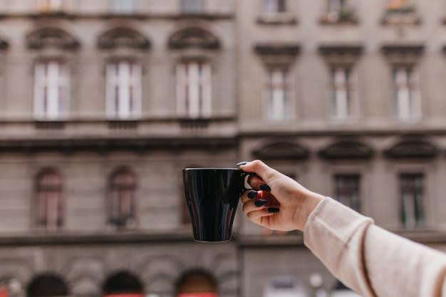 Photo of female hand with black cup of hot beverage